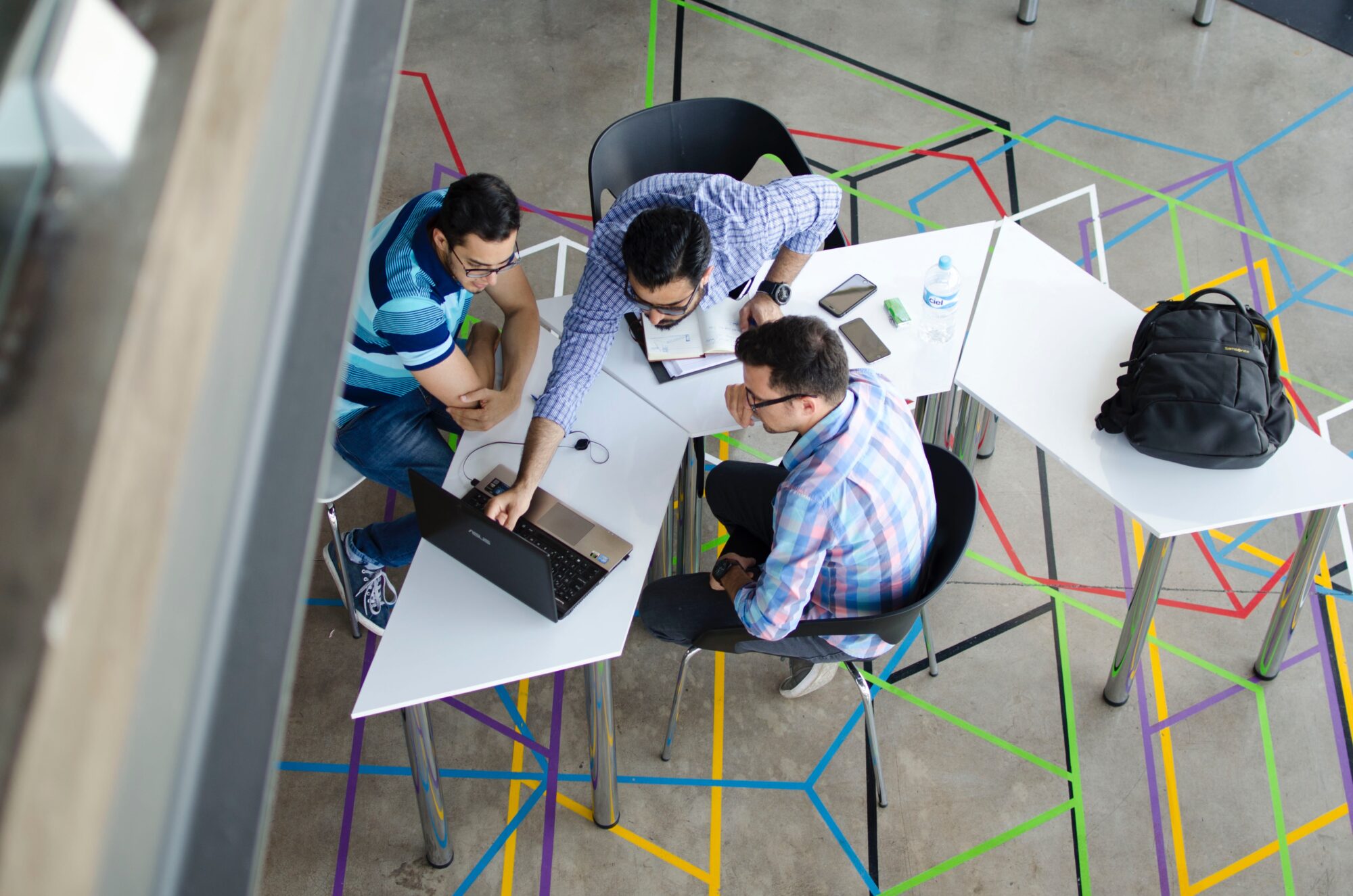 Birds-eye view of three students sat at a desk looking at a laptop